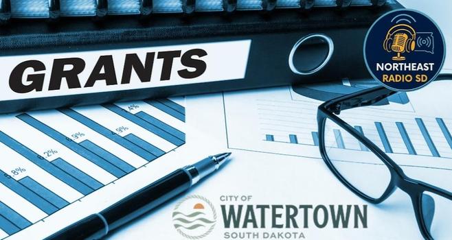 Document binder labeled "GRANTS," with charts, glasses, and a pen. Logos of Northeast Radio SD and City of Watertown, South Dakota.