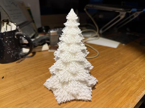 Close-up of the 3-D printed tree. It’s white, with branches made of curving filament in spiky pattern.


