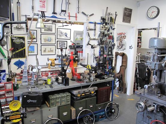 Eine sehr voll gestellte Werkbank mit Geräten, um Fahrrad Laufräder einzuspeichern. Unter der Arbeitsplatte ist alles voll mit Metallkisten und Kästen. Davor stehen mehrere fertig eingereichte Laufräder für Custom-Bromptons.
