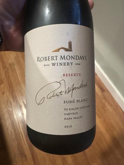 The front of a bottle of a white wine from Robert Mondavi winery. It’s a 2016 Robert Mondavi Reserve Fume Blanc from Oakville.
The graphics on the front is a gold outline of a building with a tower on the right and a prominent signature of Robert Mondavi across the label.
Scanned text:
“ROBERT MONDAVI
ESTD WINERY 1966
RESERVE
FUMÉ BLANC
TO KALON VINEYARD
OAKVILLE
NAPA VALLEY
2016”