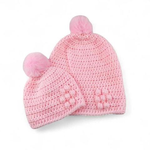 Two pink crocheted beanies with fluffy pink pom-poms and textured bubble stitch patterns, set against a plain white background.