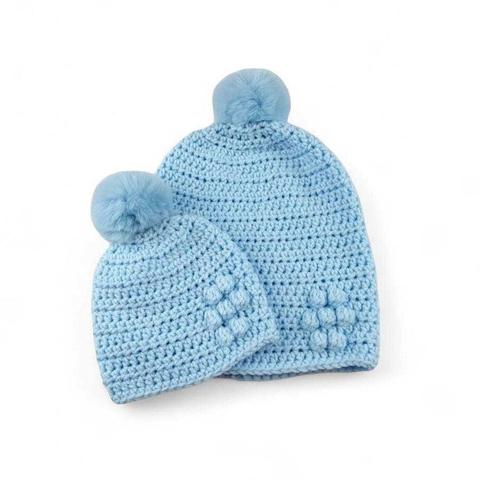 Two light blue crocheted beanies with fluffy blue pom-poms and textured bubble stitch patterns, set against a plain white background.