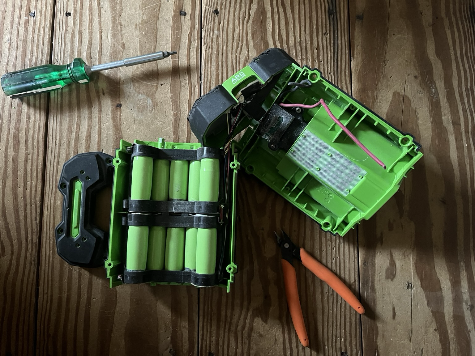 Disassembled lithium ion power tool battery pack showing cells in holders with wires attached beside a screwdriver and a pair of flush cutters