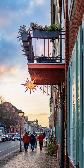 👁️ A Moravian star (Herrnhüter Stern, Star of Bethlehem) hangs from a balcony above a city street at sunset 
📍 Dutch Quarter, Potsdam
📅 14 Dec 2025
📸 Nikon D5600
⚪️ Nikkor DX 35 mm ƒ1.8G
🎞️ ISO 640, ƒ1.8, -0.3 ev, 1/4000s