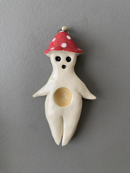 Little white porcelain humanoid mushroom figure with a white-spotted red cap and a scooped out tummy niche glazed soft yellow