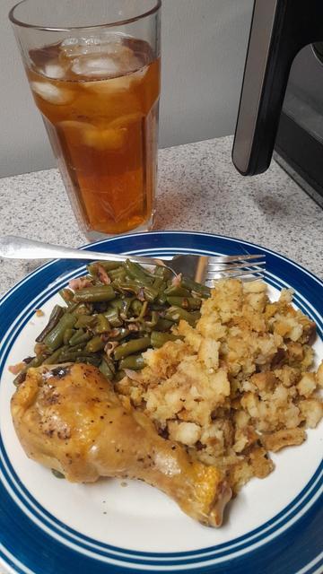 Plate with golden brown chicken, stuffing and green beans with large tea glass behind