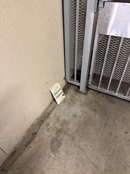 someone left a brand new book called "Atomic Habits" on the ground leaning against the wall by a security gate.