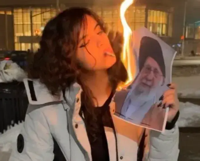 original AltTxt from Ben Royce:
a woman lighting a cigarette with a burning phot of the Ayatollah
