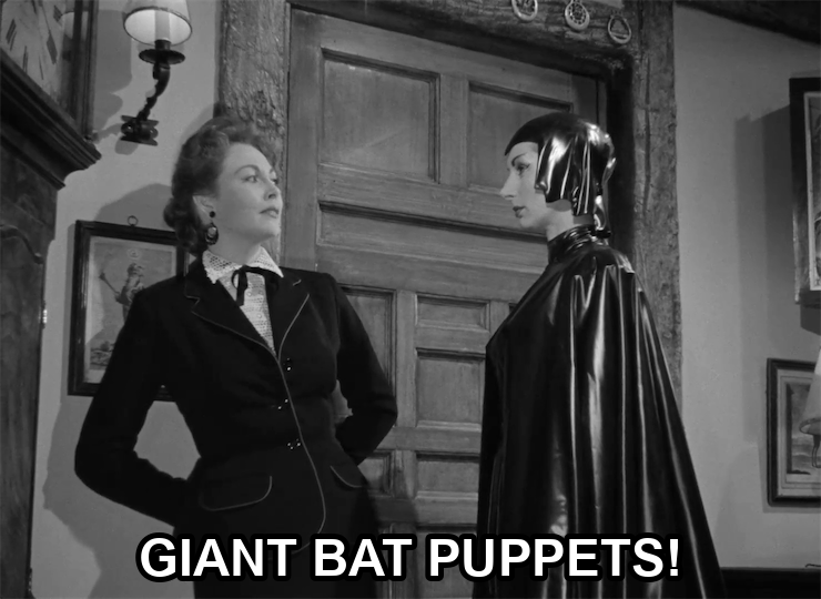 screenshot from the film Devil Girl From Mars showing a serious woman wearing a black leather suit, cape, and cowl. Superimposed text says: "Giant bat puppets!"