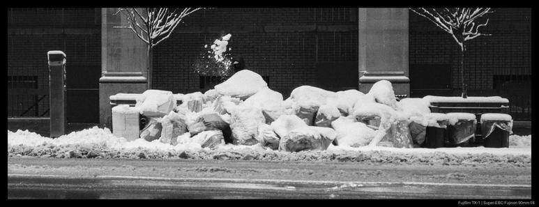 A building worker shovels snow onto a large curbside pile of garbage bags after a snowfall in New York City.