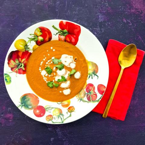 Bowl of harissa spiced aubergine (eggplant) and tomato soup topped with a swirl of cream and fresh herbs.