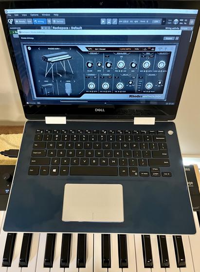 Blue laptop running Rhodes Anthology virtual instrument software and sitting on top of a MIDI keyboard controller.