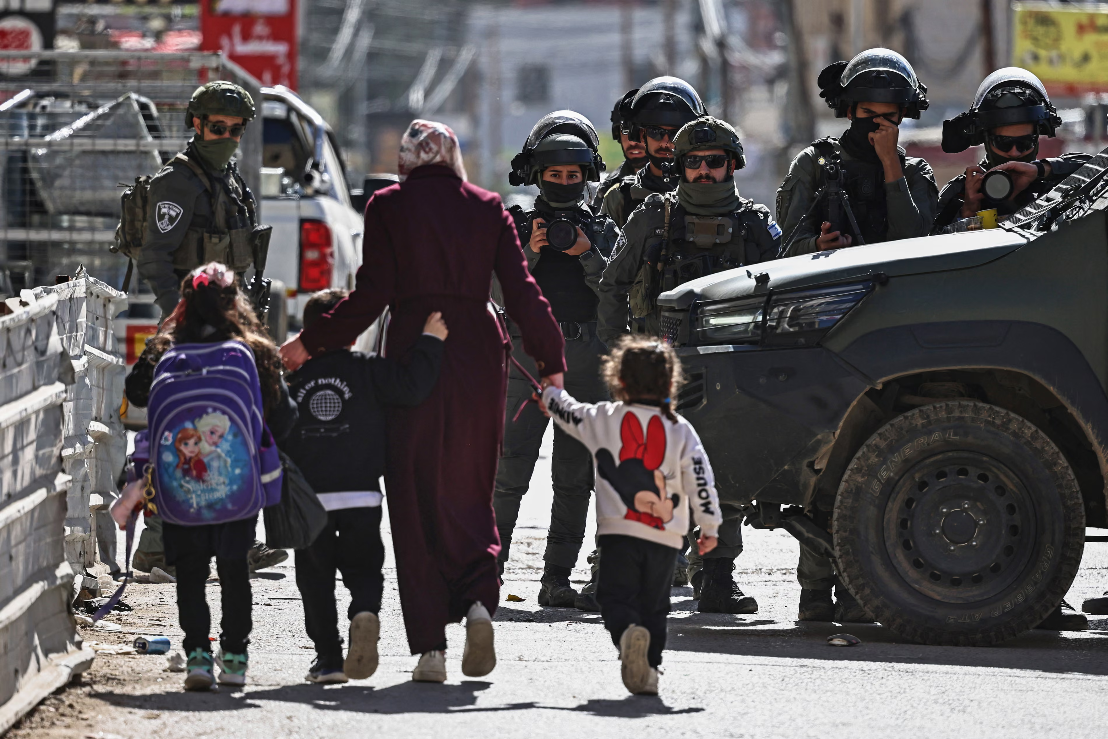 A woman and children walk past members of the Israeli security forces near Ramallah in the Israeli-occupied territory.