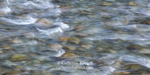 A shallow river running over colourful rocks resting at the bottom.