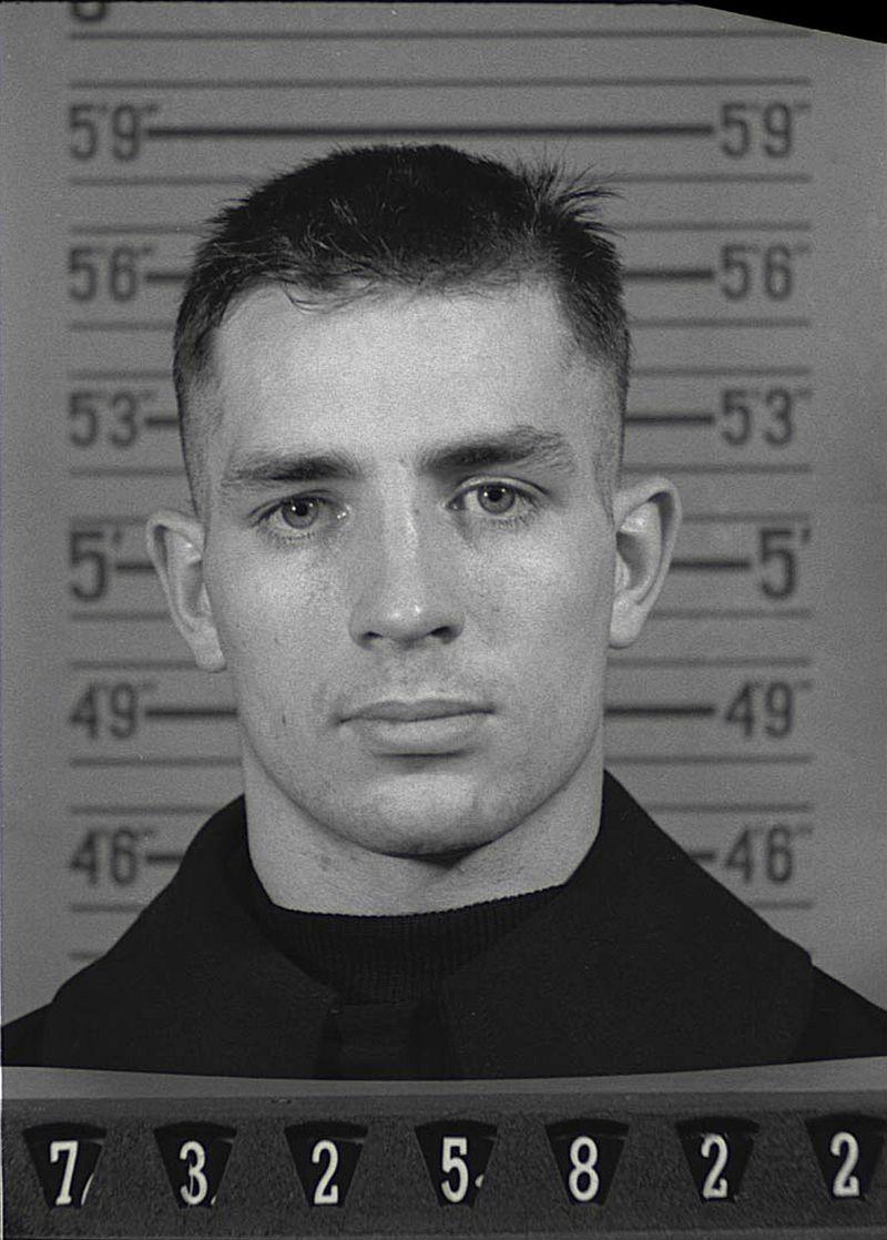 Naval Reserve Enlistment photograph of Jack Kerouac.- picryl.com. He standing in front of a height chart. (He is 5'9".)  At the bottom of the photo is his enlistment number.