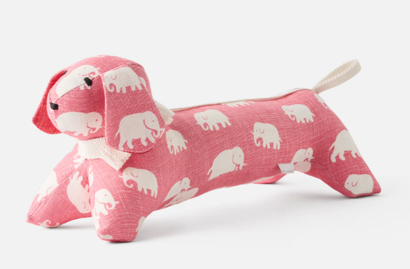 Ein rosa Kissen in Form eines Dackels, mit weißen Elefanten bedruckt. 