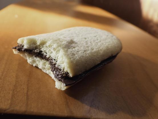 A piece of a sandwich cookie: pale pastry on top and bottom with a chocolate layer in the middle.  The broken edge shows the fine crumb of the pastry. 