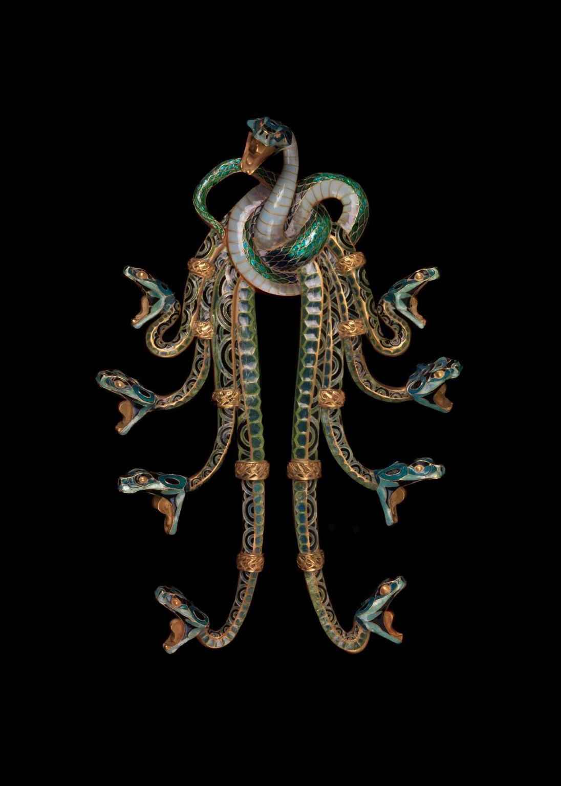 official museum photo of the serpent pectoral, front profile on black background “This piece can be considered one of the paradigms of Lalique’s jewellery production, both for the mastery of its execution and the choice of theme. Reptiles were, indeed, a frequent source of inspiration for the artist throughout his career, a motif to which he constantly returned, both in the jewellery of the Art Nouveau period and in the glass production of the Art Deco period. The nine intertwined serpents that make up the corsage ornament, in stained glass enamel and enamelled gold, form a knot from which the bodies of eight of them cascade down, with the ninth rising up in the centre at the top of the jewel. The heads of the reptiles, in attack position, have open mouths from which rows of pearls may have hung. A piece of jewellery whose whereabouts today are unknown and of which this is probably the only replica, featured prominently at the 1900 Paris Exposition.”