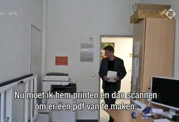 Man loopt met papier naar printer met de tekst: nu moet ik hem printen en dan scannen om er een pdf van te maken.