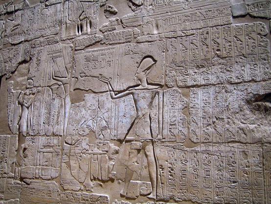 photograph of Egyptian hieroglyphs with a central figure seemingly lecturing others. Photo attribution: Flickr user tonayo