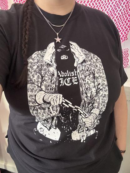A woman wearing a t shirt showing a menacing character holding a chain and who is in turn wearing an "Abolish ICE" shirt