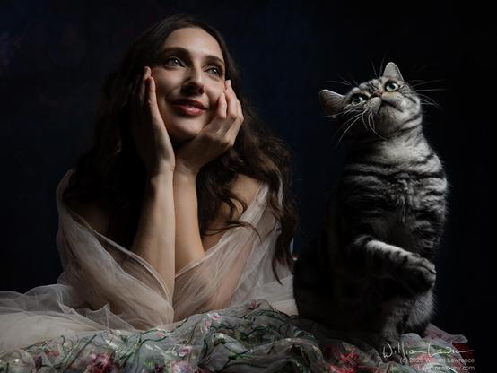 Model Anoush Anou poses leaning on a table, wrapped in chiffon, staring wistfully off into the distance. She is joined by cat CJ, who stares off into the distance with her.