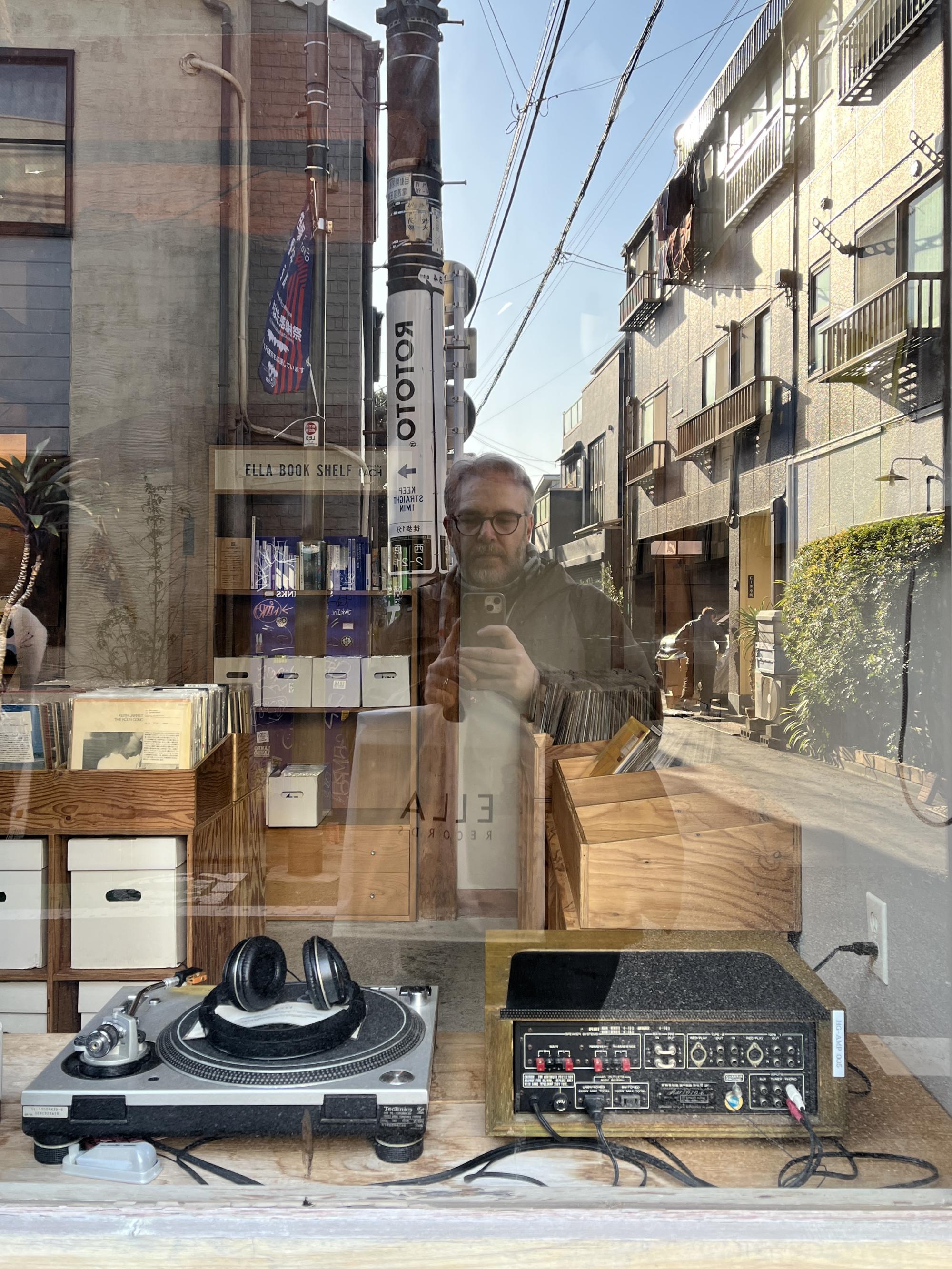 Me reflected in the window of Ella Records, Hatagaya, with Technics deck and amp in foreground, records and reflected street behind.