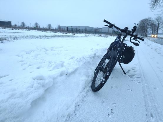 Geparktes Fahrrad auf dem Radweg. Auf dem Radweg ist eine ganz dünne Schneeschicht. Links und rechts sind noch die Reste der Schneewehen von vor einer Woche.