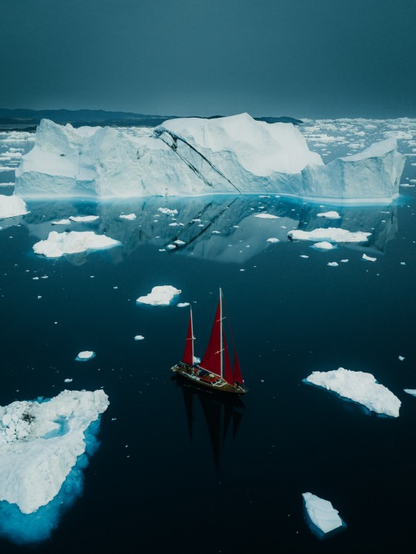 A red sailing boat amongs breaking up icebergs.