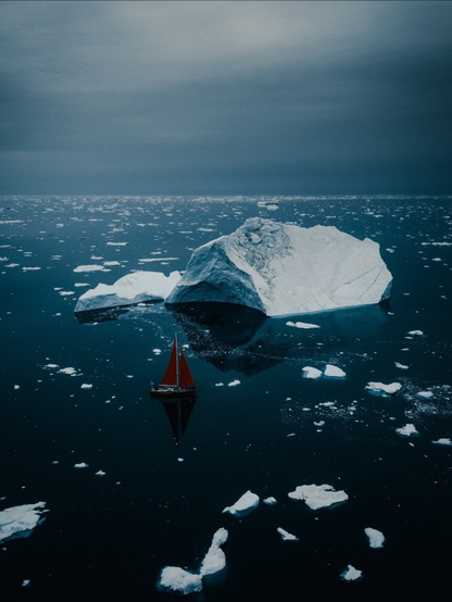 A red sailing boat amongs breaking up icebergs.