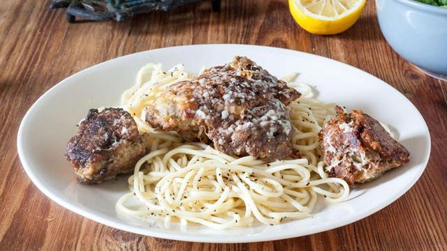 Chicken and artichokes with lemon sauce atop a plate of pasta.