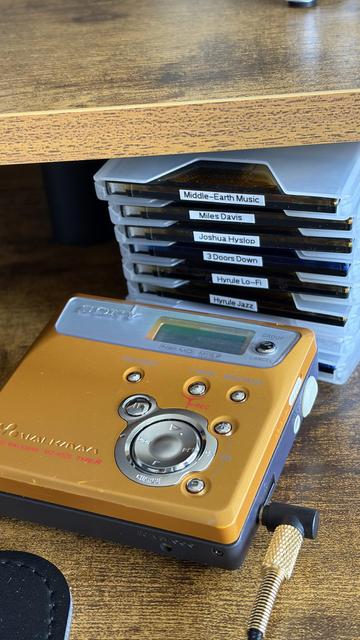 A real photo of a gold colored minidisc Walkman with a stack of minidiscs behind it.