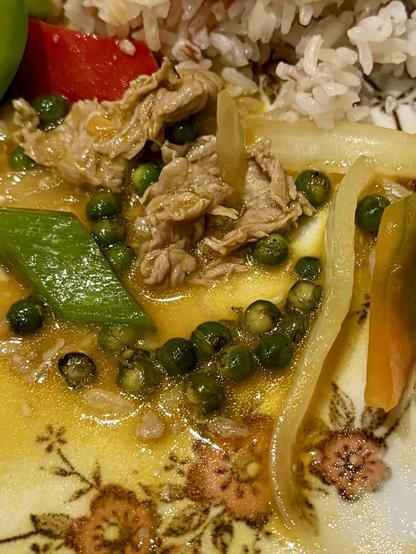 Close-up of a plate with rice, stir-fried beef and vegetables in an orange, fruity sauce and many green peppercorns.