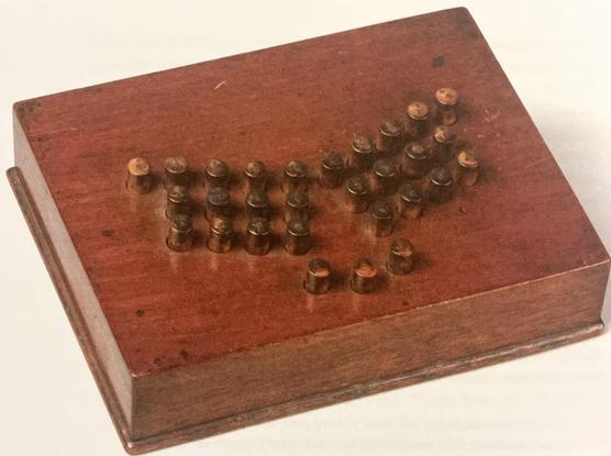 Flat wooden box about the size of a laptop case. With round wooden buttons on top. Buttons split in two groups, one for each hand, like a modern ergonomic keyboard. With three buttons centered below for the thumbs.
