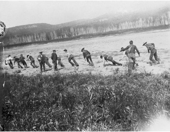 Men hauling a boat upriver with lines, while the guide yells haul, haul, and the gentlemen watch.