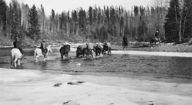 Men on horseback lead packhorses through the wilderness north of Edmonton House.