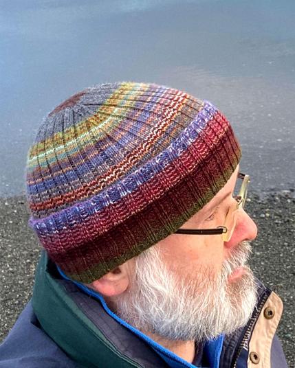 Side view. Wearing a ribbed cap knit from leftover yarn at Jackson Beach on San Juan Island WA. A wide variety of colors are knit helically for an overall warm, cozy effect.