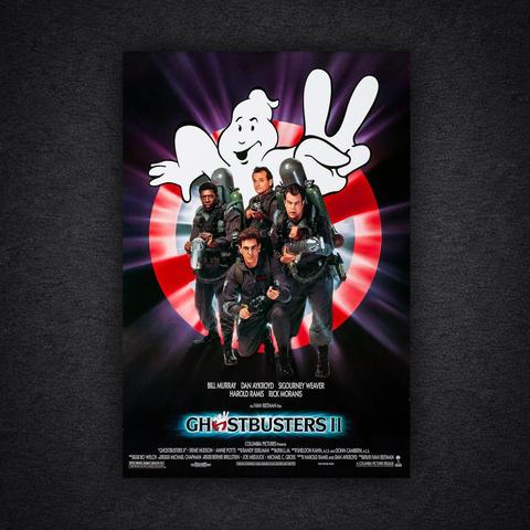 The theatrical poster for Ghostbusters II on a dark textured background. Four Ghostbusters in grey jumpsuits and proton packs stand together holding equipment, with Bill Murray at the front. Behind them is the red “no ghost” logo, with a white cartoon ghost emerging and holding up two fingers in a peace sign. The film title “Ghostbusters II” appears at the bottom, with cast names including Bill Murray, Dan Aykroyd, Sigourney Weaver, Harold Ramis, and Rick Moranis.