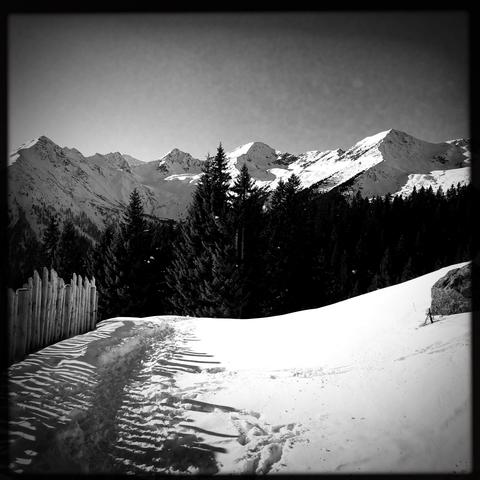 Una sentiero battuto nella neve con uno steccato in legno sulla sinistra e le cime delle montagne innevate in lontananza