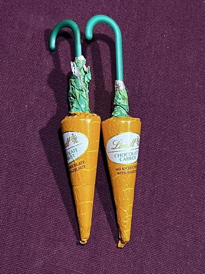 Picture of Lindt Chocolate Carrots, little conical shaped chocolates, wrapped in orange wrapper with green at the ends with a stick sticking out of them that ends in a hook, which really ends them up, looking like umbrellas, since carrots don’t have curves at the end anyway.
They’re sitting on a red cloth background and they’re really really really really really old and either I should throw them away or eat them.
And honestly, they’re old enough that I probably should just throw them away.
…