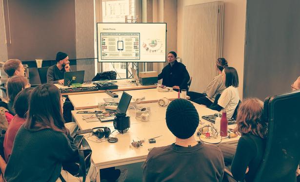 Students sitting at a table full of electronic waste and watch a presentation about smartphone components