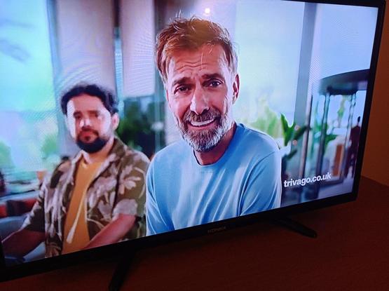 A still from a Trivago commercial with a bearded white man wearing a white T-shirt.