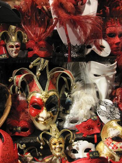 Eine Auswahl an venezianischen Masken in Rot, Schwarz und Weiss mit Federn und Spitzen und Glitzer. Einige sind komplette Masken andere nur für die Verdeckung der Augen. Gesehen in Venedig in einem Schaufenster.