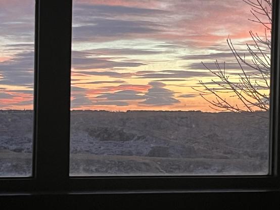 Winter sunset of many colors through window with tree branches right