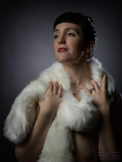 Model Ars Corporealis poses standing nude, draped strategically in a (faux) fur stole.