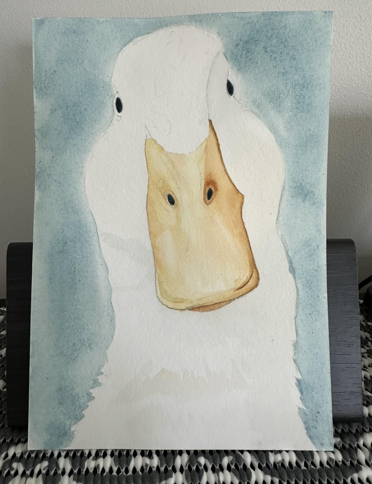 A watercolor painting of a duck face facing forward with a yellow-orange beak and a light blue background