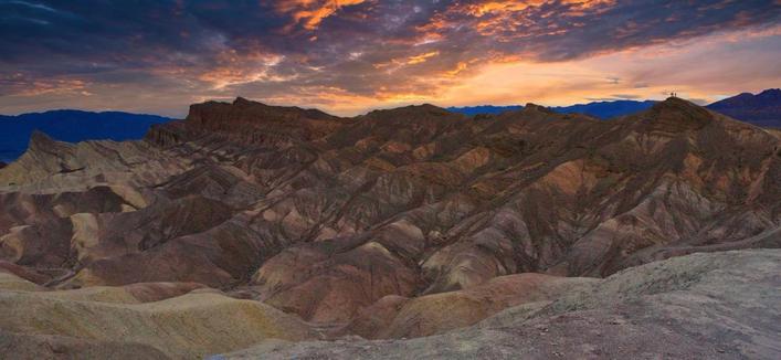 Sunset behind mountains with three people standing on top of one of the mountains