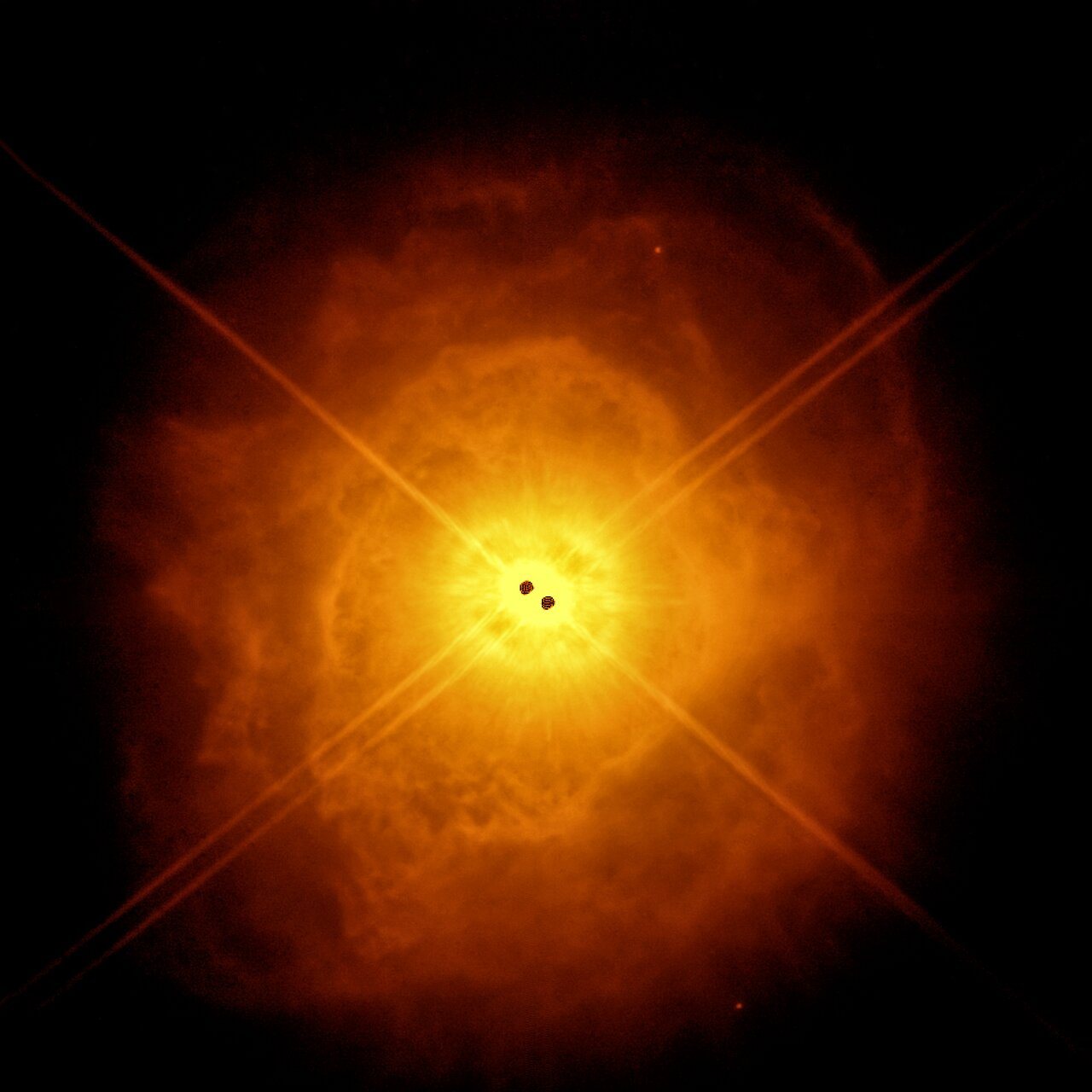 An orange nebula with a cloud-like texture against a black background. The nebula is more yellow-orange and opaque at the centre and darker-orange and more diffuse at its perimeter. At the centre of the image inside the nebula there are two small black dots.