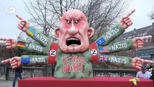 A Putin sculpture pointing to 6 other nations claiming they are all nazis while he himself is wearing a military uniform and a red armband with a Z that also looks a lot like an N.
