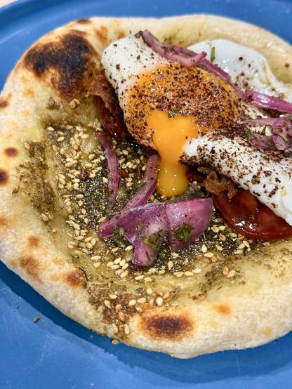 A zaatar manouche with a dripping egg yolk and sumac onions on a blue plate. 